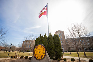 The sun shines brightly over a flag pole and the CMU seal