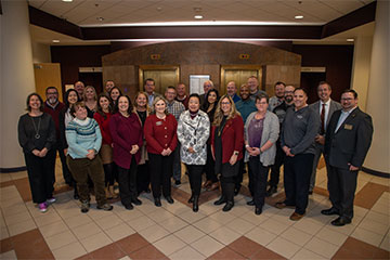 A group of people in business casual dress pose for a group photo in a building lobby.