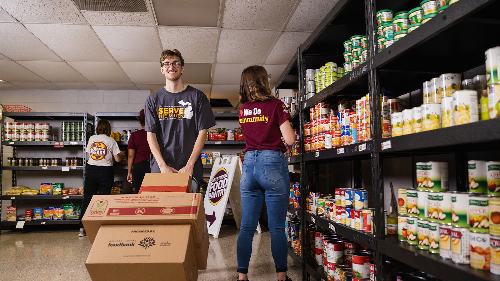 A student volunteering at a food pantry unloading boxes of canned goods and produce.