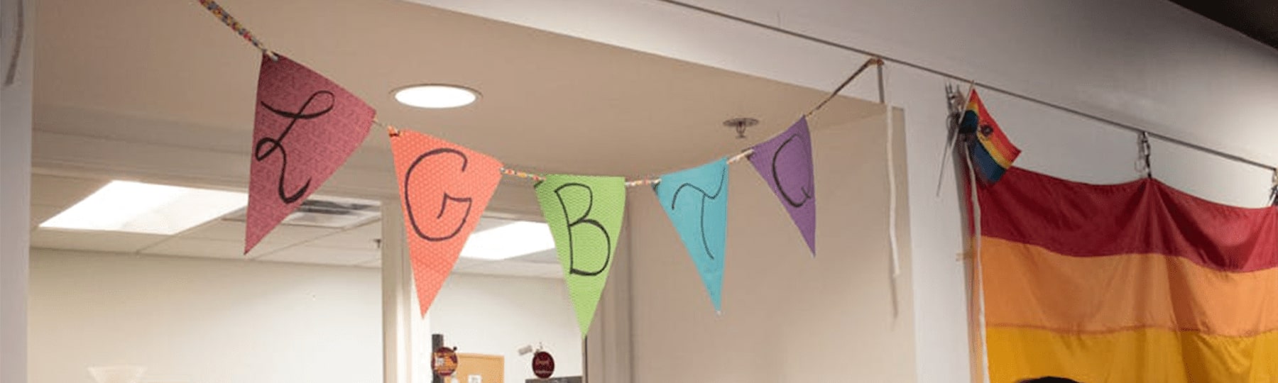 A multicolored pennant flag hangs above an office door, with the letters LGBTQ on each flag