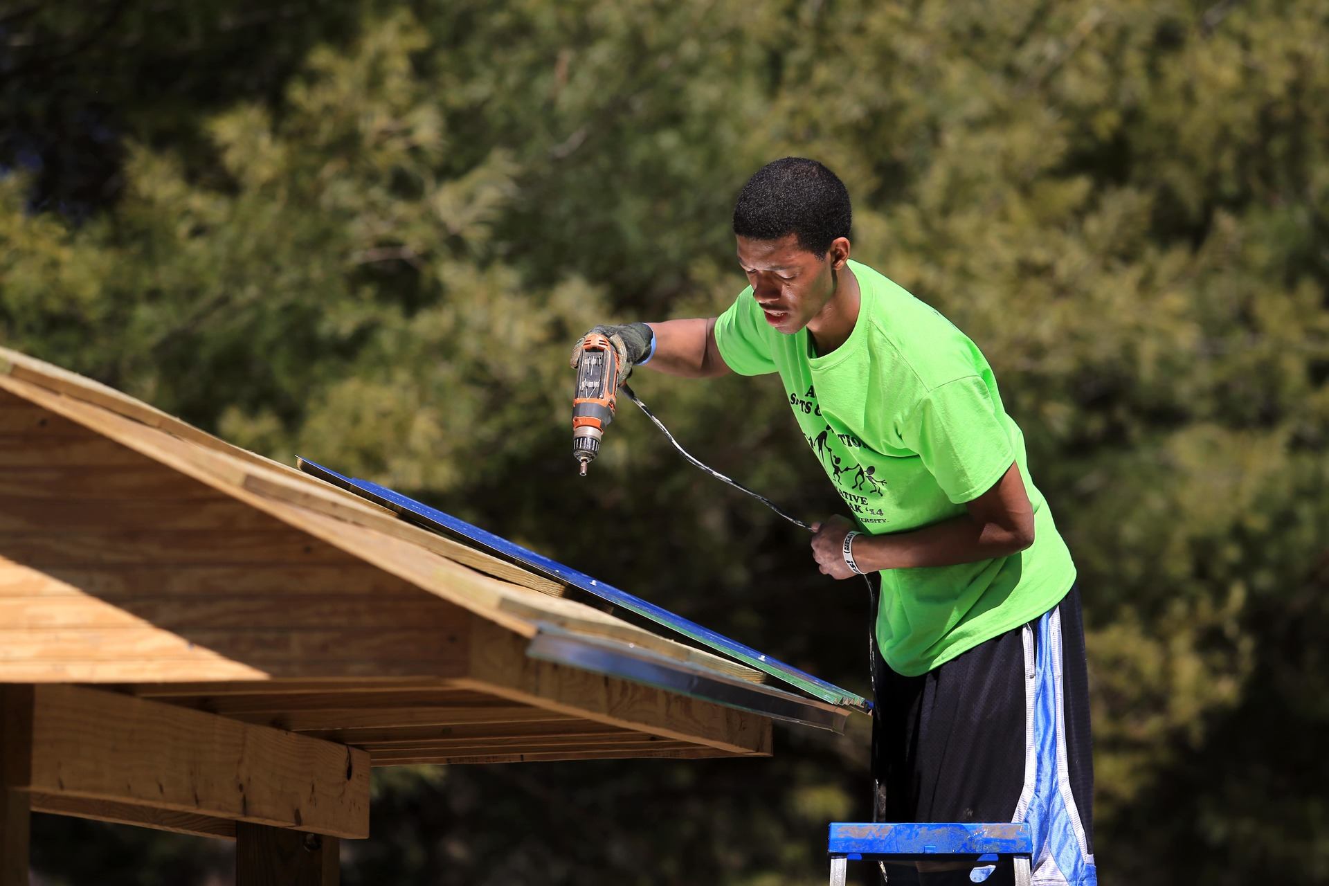 A student holds a drill while standing on a ladder during an Alternative Break in Asheville.