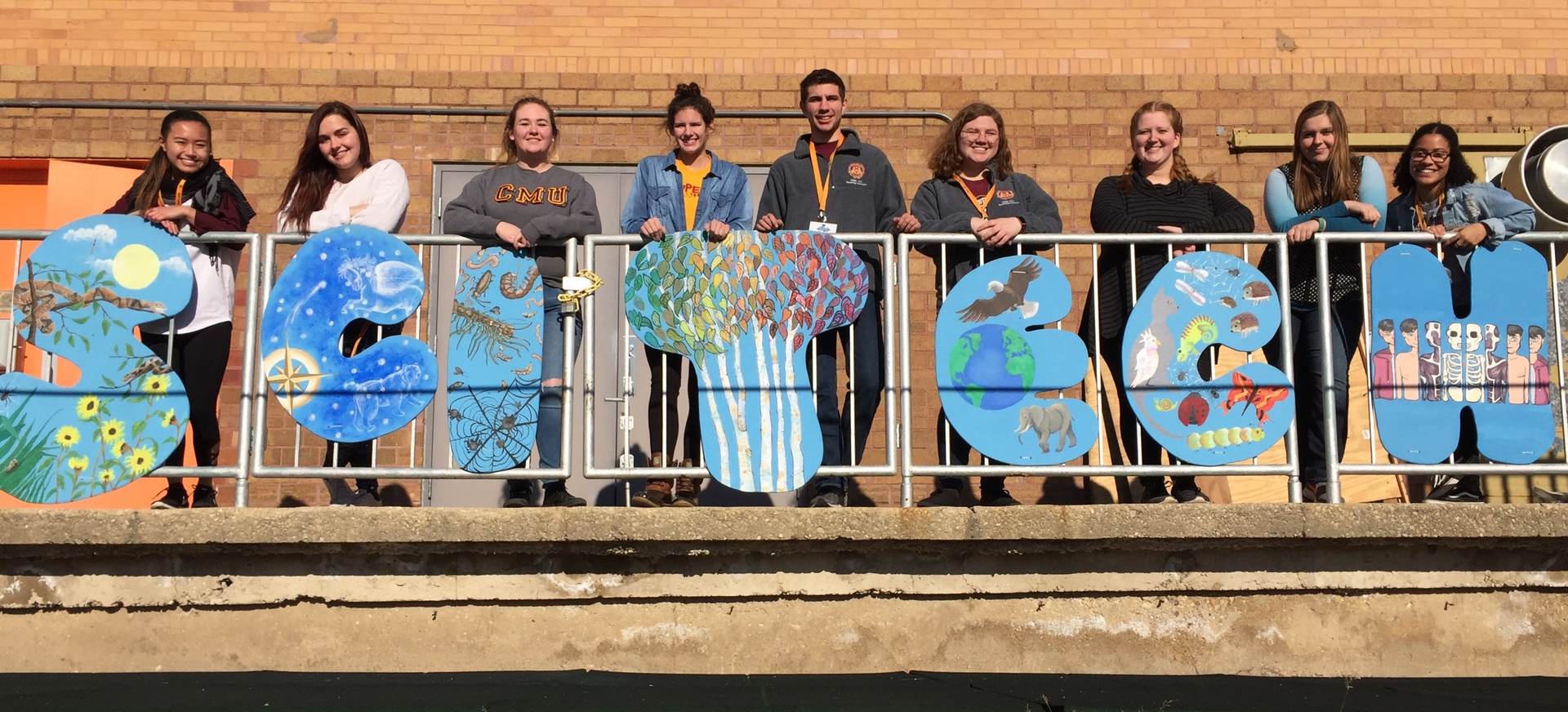 A group of students on a balcony holding up letters that spell "SciTech."