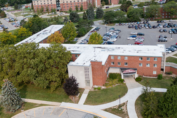 Aerial view of Beddow Hall on the campus of Central Michigan University, captured from a drone. The residence hall is surrounded by lush green grass and trees, with clear blue skies above.