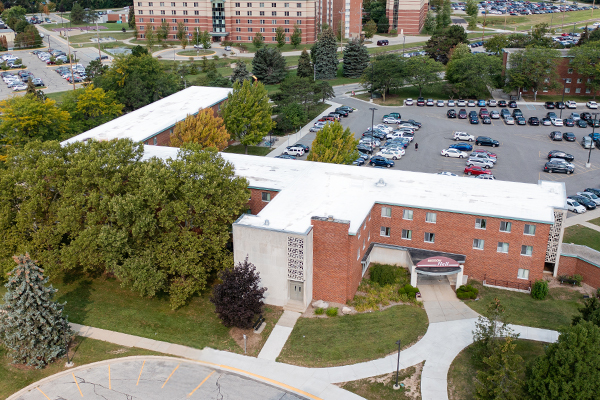 Aerial view of Beddow Hall on the campus of Central Michigan University, captured from a drone. The residence hall is surrounded by lush green grass and trees, with clear blue skies above.