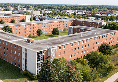 Aerial view of Herrig Hall on the campus of Central Michigan University, captured from a drone. The residence hall is surrounded by lush green grass and trees, with clear blue skies above.