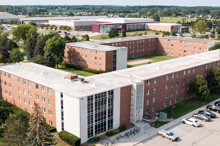 Aerial view of Saxe Hall on the campus of Central Michigan University, captured from a drone. The residence hall is surrounded by lush green grass and trees, with clear blue skies above.