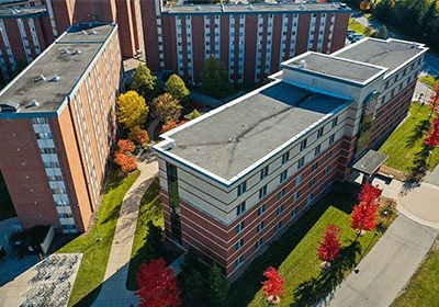 Aerial view of Wheeler Hall on the campus of Central Michigan University, captured from a drone. The residence hall is surrounded by lush green grass and trees, with clear blue skies above.