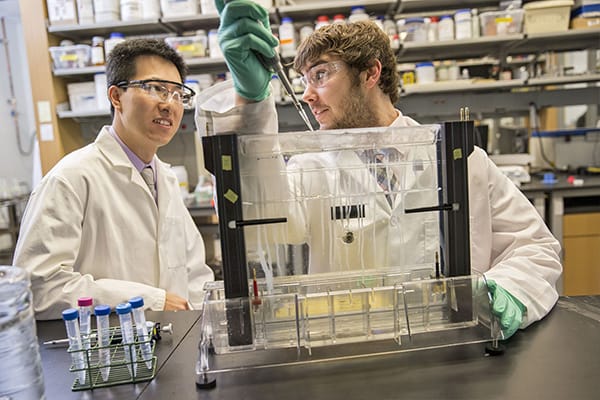 Two students wearing lab coats work in a biochemistry lab on campus at Central Michigan University.