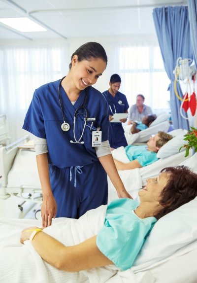 A woman in medical clothing smiling while helping a woman in a hospital bed.