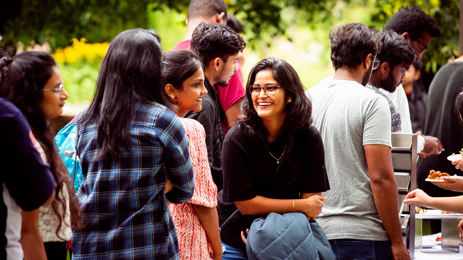 A student smiles and talks with other students while waiting in line for food at an outdoor event.
