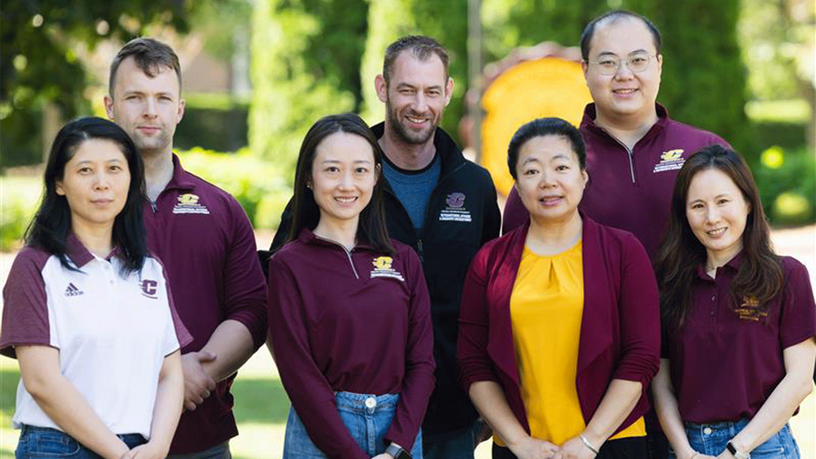 A group photo of the International Admissions team as they stand together wearing maroon and gold outside in front of Warriner and the gold CMU seal.