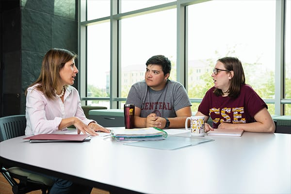 A female staff member talks with two students wearing CMU shirts.