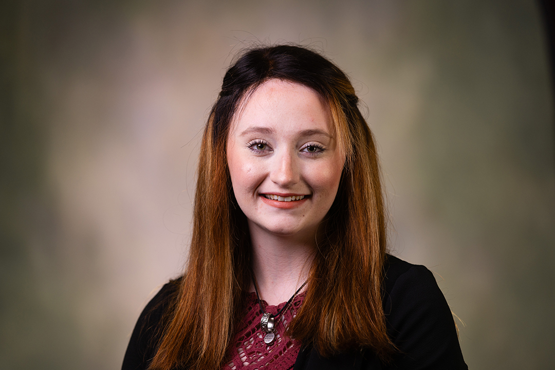 Professional headshot of Sydnee Sutliff wearing a black blazer and maroon shirt while looking at the camera.