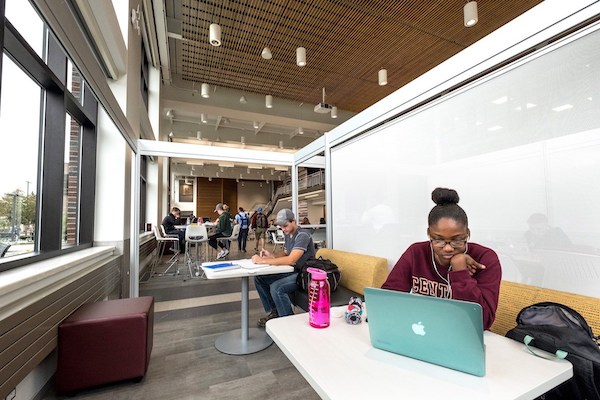 A student in a maroon CMU sweatshirt works on a laptop with a teal cover in the College of Business Administration.