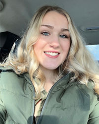 SI Leader for CSD 278, Emily Avery, smiles for a headshot inside of a car while wearing a green jacket.