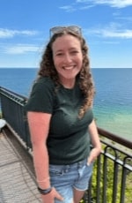 A woman standing on a balcony with a railing and water in the background.