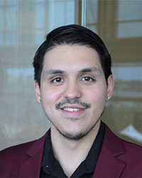 Headshot of Alumni Association Board of Directors member Kevin Bautista-Mancilla wearing a maroon blazer over a black collared shirt and he has short black hair and is smiling with teeth.