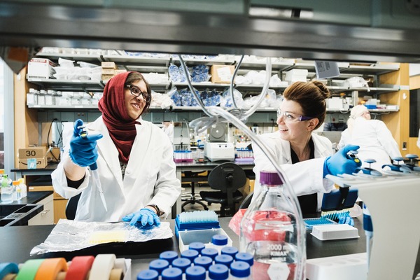 A CMU student and faculty member wearing lab coats and glasses, conducting experiments in a lab.