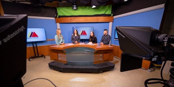 Four students sitting behind the desk at News Central.