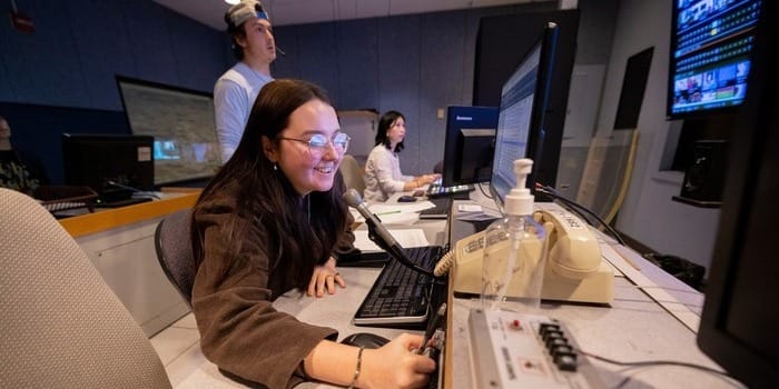 Students at a desk in a broadcasting studio, producing a live newscast.