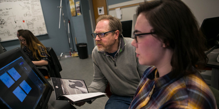 Student and faculty member work together at a computer in a classroom.