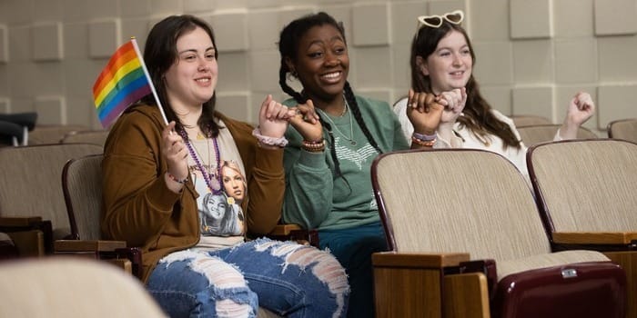 Students sitting together in chairs, cheering at a diversity and inclusion event.