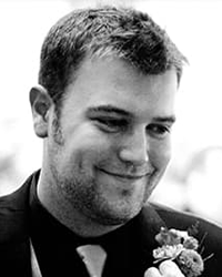 David Bone's headshot for Alumni Awards that is black and white with him wearing a suit having a boutonniere pinned onto him.