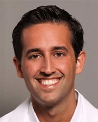 Nicholas Cozzi updated headshot with smiling with teeth with black hair wearing a white collared shirt.