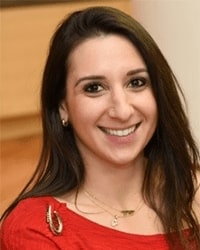 Sharon Elefant's headshot for the Alumni Awards where she is wearing a bright red top and is smiling with teeth with long dark brown hair.