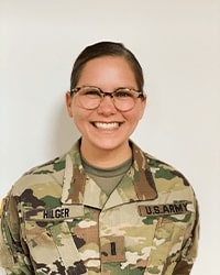 Mary Hilger's headshot for the Alumni Awards wearing a army uniform and glasses with brown hair pulled back into a bun while smiling with teeth.