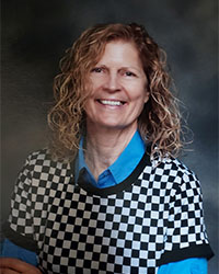 Headshot of 2024 Alumni Award Honorary Alumni Recipient Audrey Zavodsky-Fraser wearing a bright blue collared shirt under a black and white checkered vest and she has shoulder length curly blonde hair and is smiling with teeth.