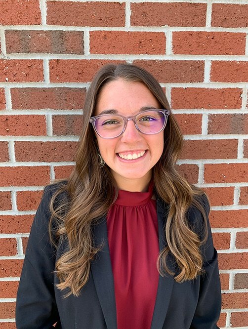 A woman smiling at camera in front of a brick wall.