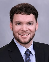 This is a professional headshot of Sean Spaniol wearing a suit and tie.