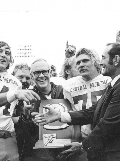 A black and white photo of CMU coaches and football players celebrating and holding a trophy.