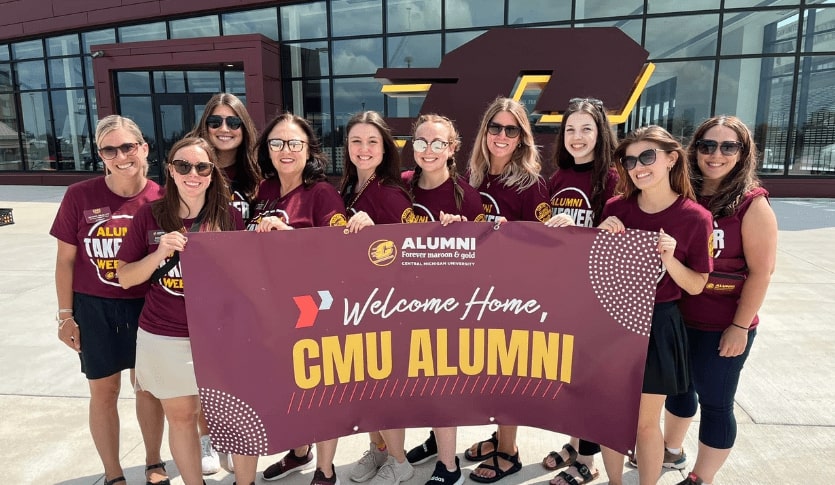 A group of women holding a maroon banner that says 