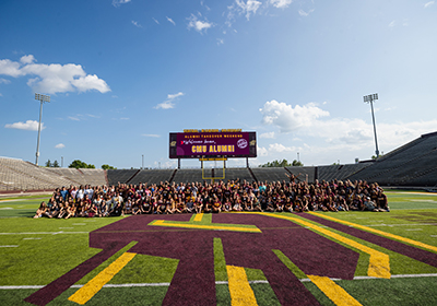 CMU alumni from the 90s and 2000s on football field for a group photo.