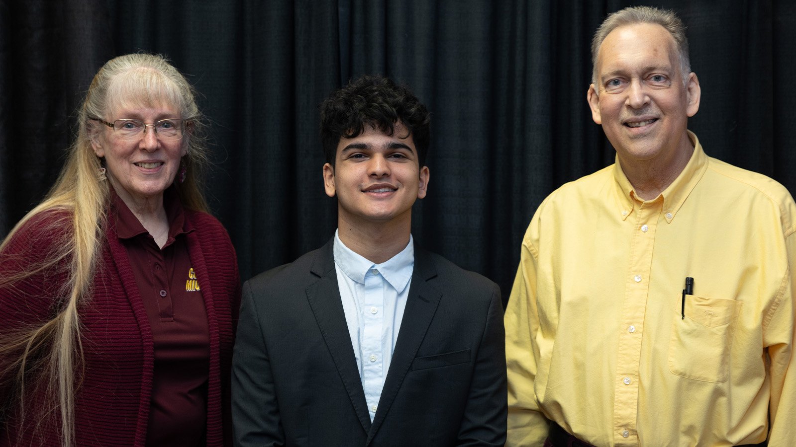 Two scholarship donors pose for a photo with the student recipient standing between them.