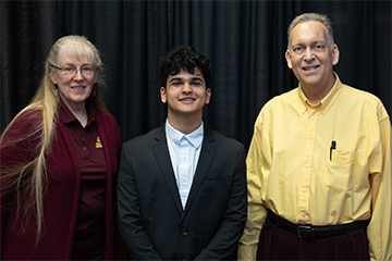 Two scholarship donors pose for a photo with the student recipient standing between them.