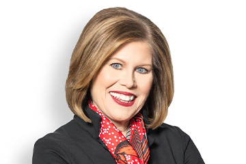 A headshot of a woman with neck-length straight brown hair smiles while wearing a black blazer and red scarf with white dots.